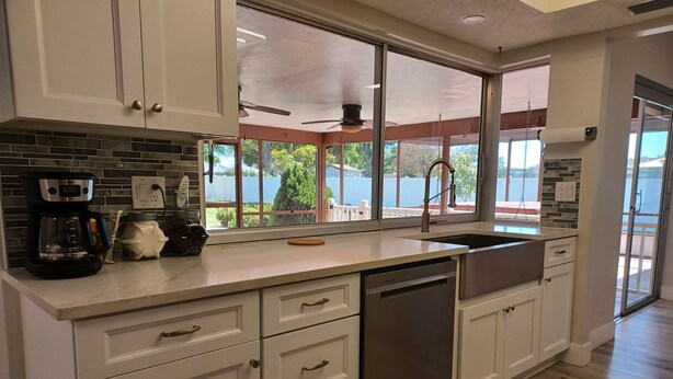 A modern kitchen with white cabinets, a stainless steel dishwasher, and a large window offering a view of greenery outside. - Spacious 3-bedroom house with HOT TUB and MOVIE THEATRE 8 minutes from RACEWAY (Sebring)
