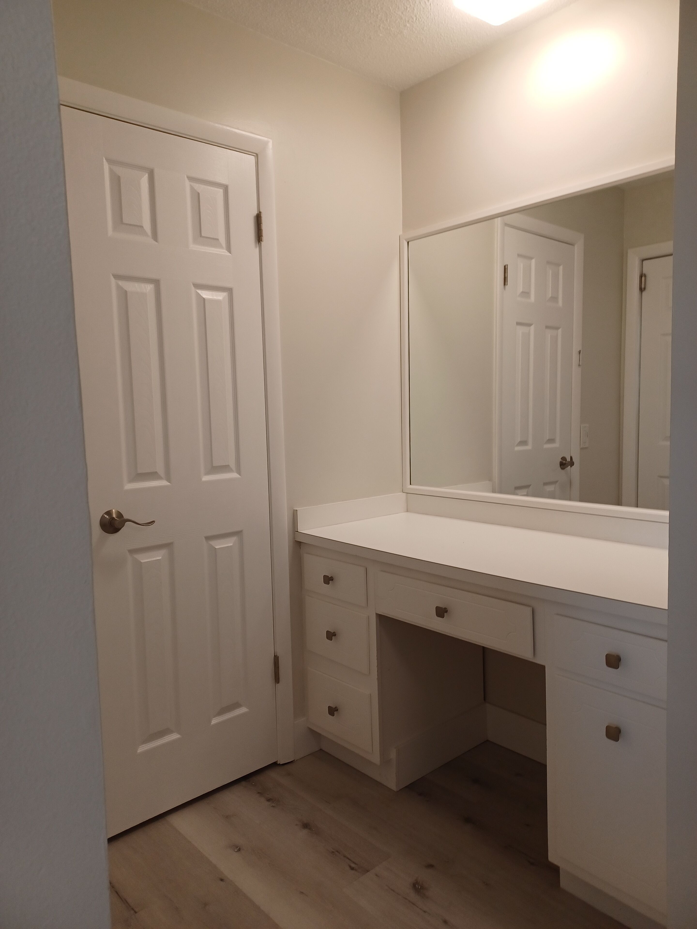 Un bagno con un mobile lavabo bianco, uno specchio e una porta.