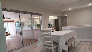 A dining area with a table and chairs, a sliding glass door leading to a balcony, and a kitchen in the background. - Spacious 3-bedroom house with HOT TUB and MOVIE THEATRE 8 minutes from RACEWAY (Sebring)