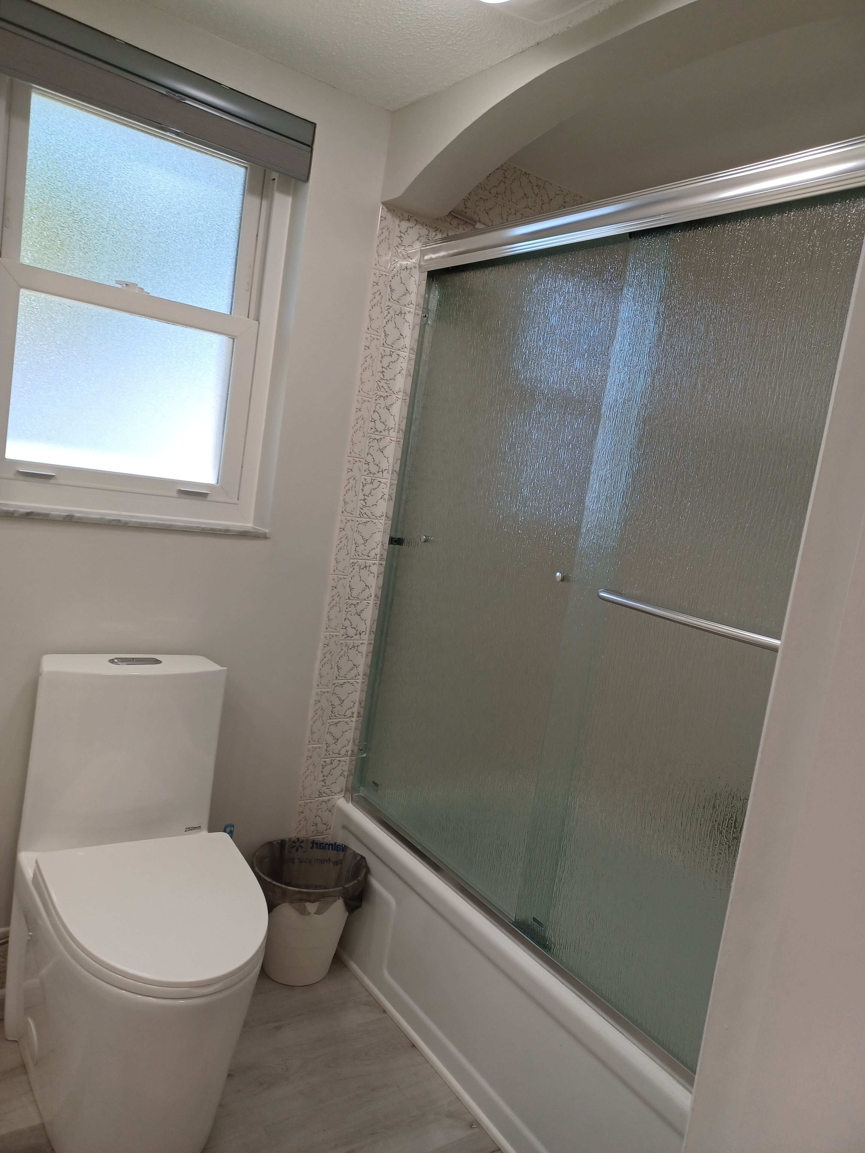 A bathroom with a toilet, a shower with a glass door, and a window.