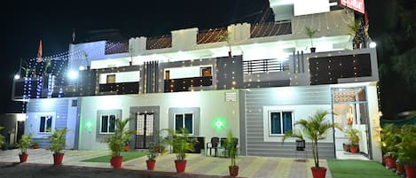 A two-story hotel with a modern design, featuring a signboard, multiple windows, and potted plants.