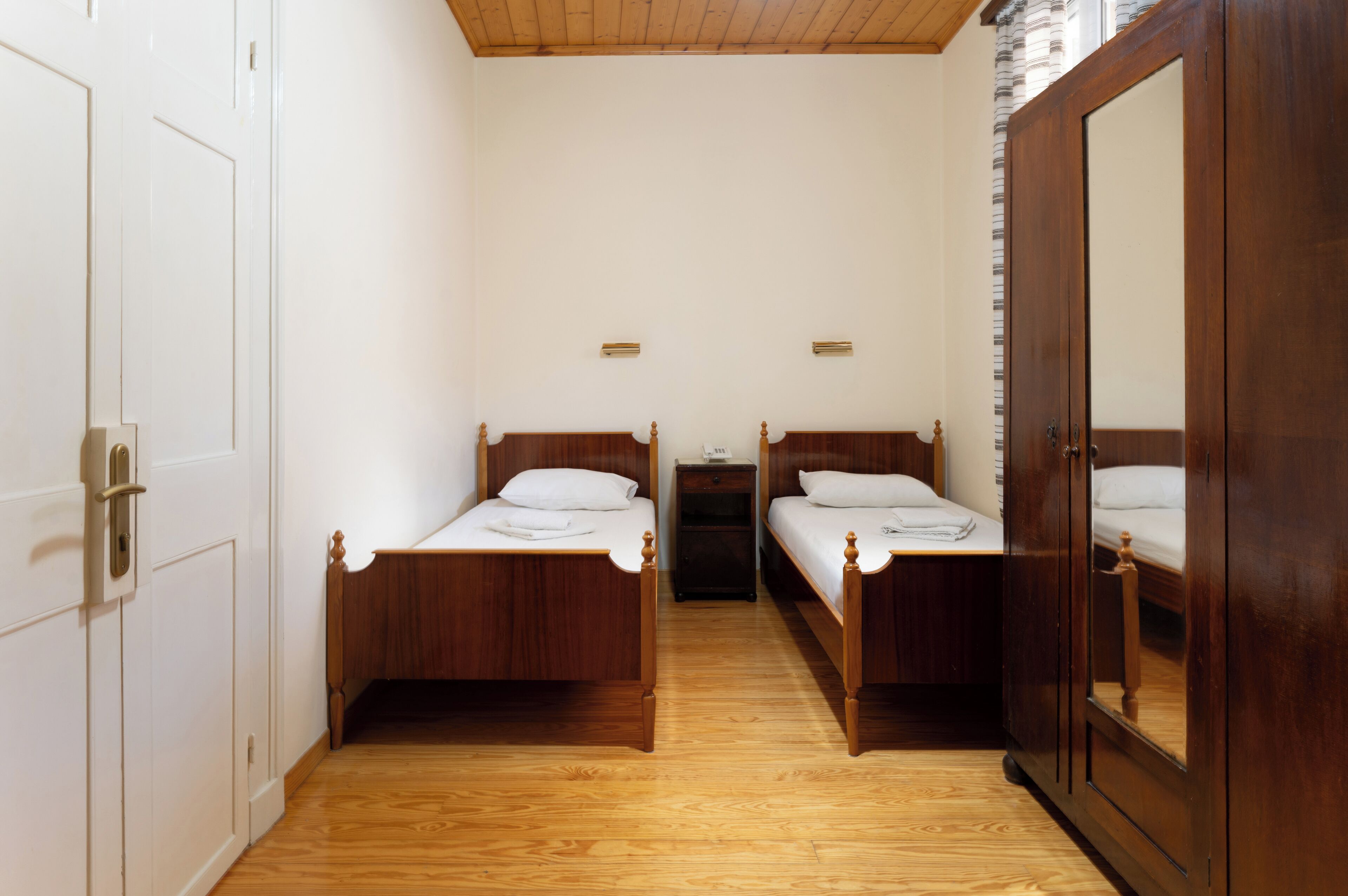 Una habitación con dos camas de madera, un armario y una mesita de noche.