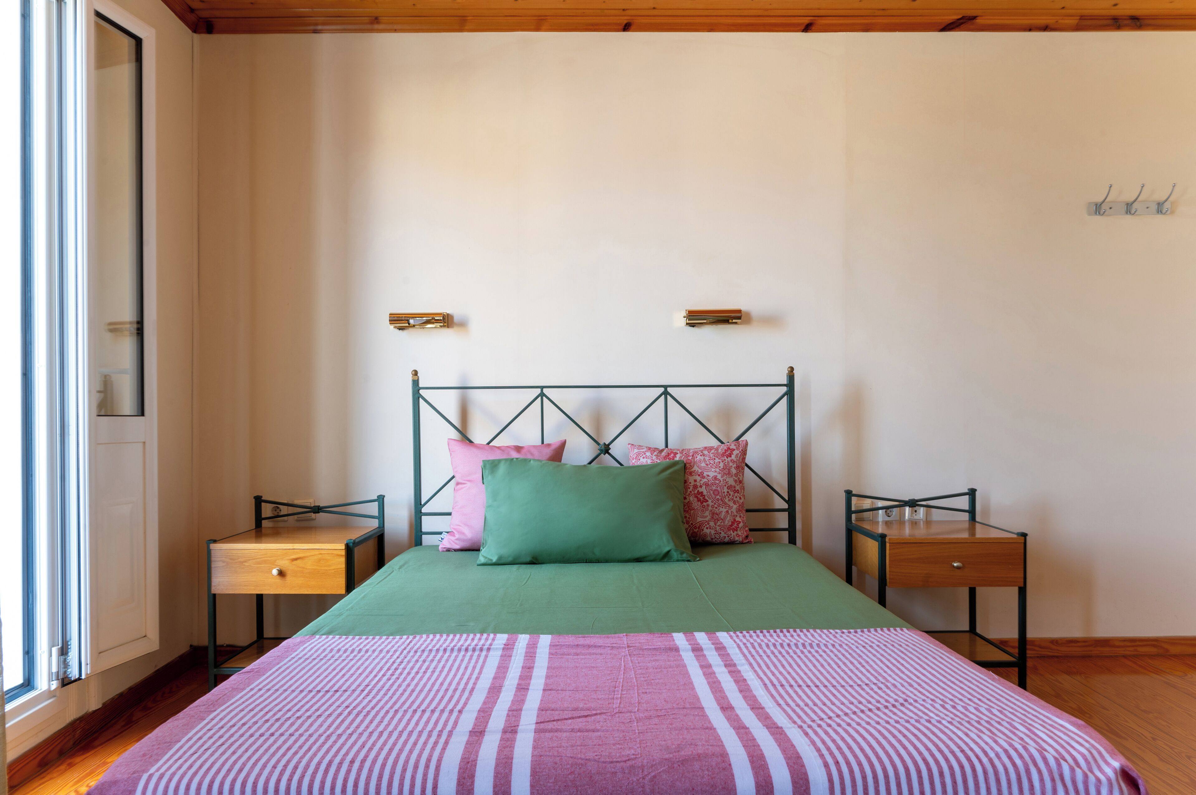 Un dormitorio con una cama, dos mesitas de noche, una ventana y una estantería en la pared.