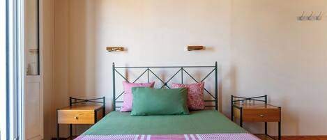 Un dormitorio con una cama, dos mesitas de noche, una ventana y una estantería en la pared.