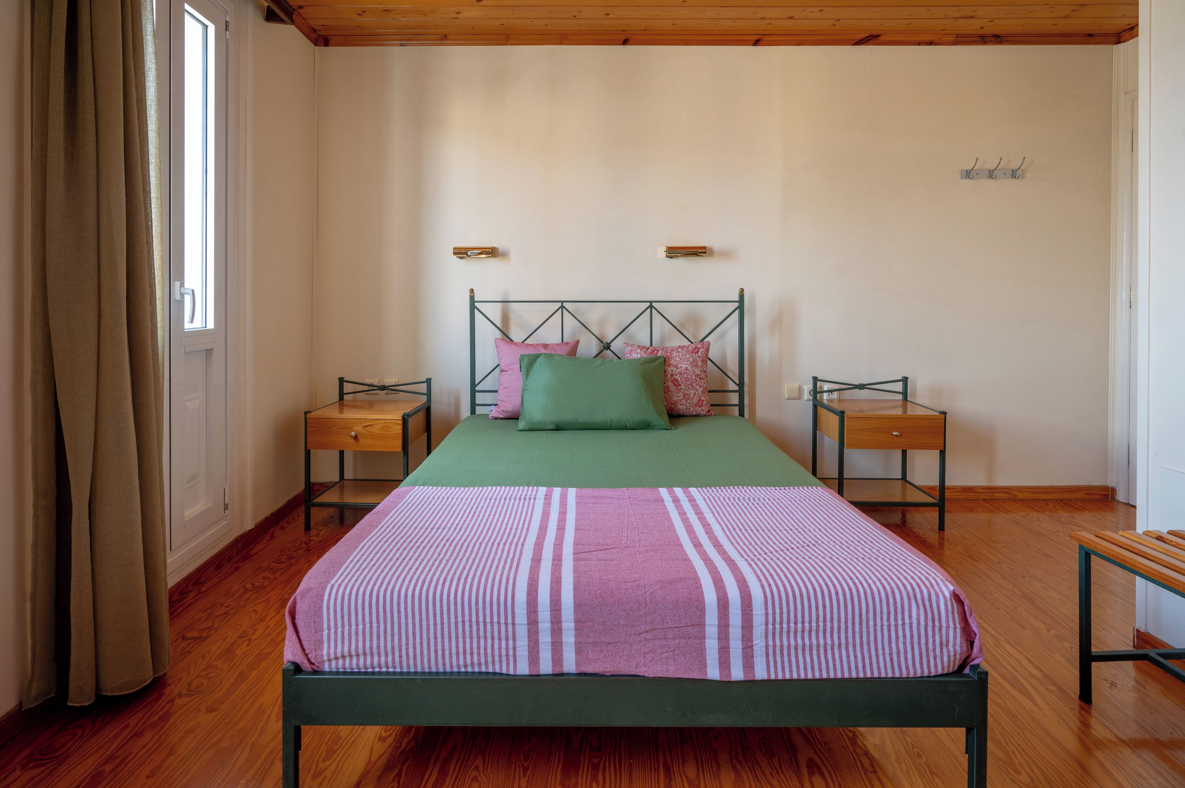 A bedroom with a bed, two bedside tables, a wooden bench, and a window with curtains.
