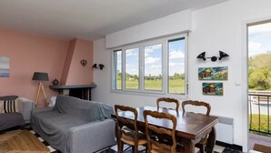Una sala de estar con un sofá, una mesa con sillas, una lámpara y un ventanal con vistas al exterior.