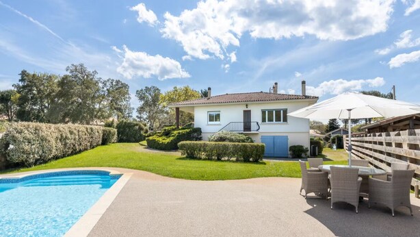 Una casa con piscina, un patio con mobiliario exterior y un jardín bien cuidado.