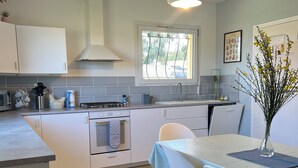 Una cocina moderna con armarios blancos, un ventanal y un comedor con mesa y sillas.