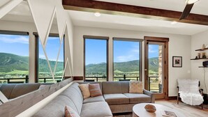 Een moderne woonkamer met een modulaire bank, een ronde salontafel en grote ramen met uitzicht op het landschap.