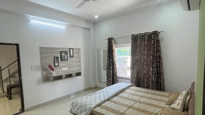 Een slaapkamer met een bed, een plafondventilator, een airconditioningapparaat, een raam met gordijnen en een trap naar een andere kamer.