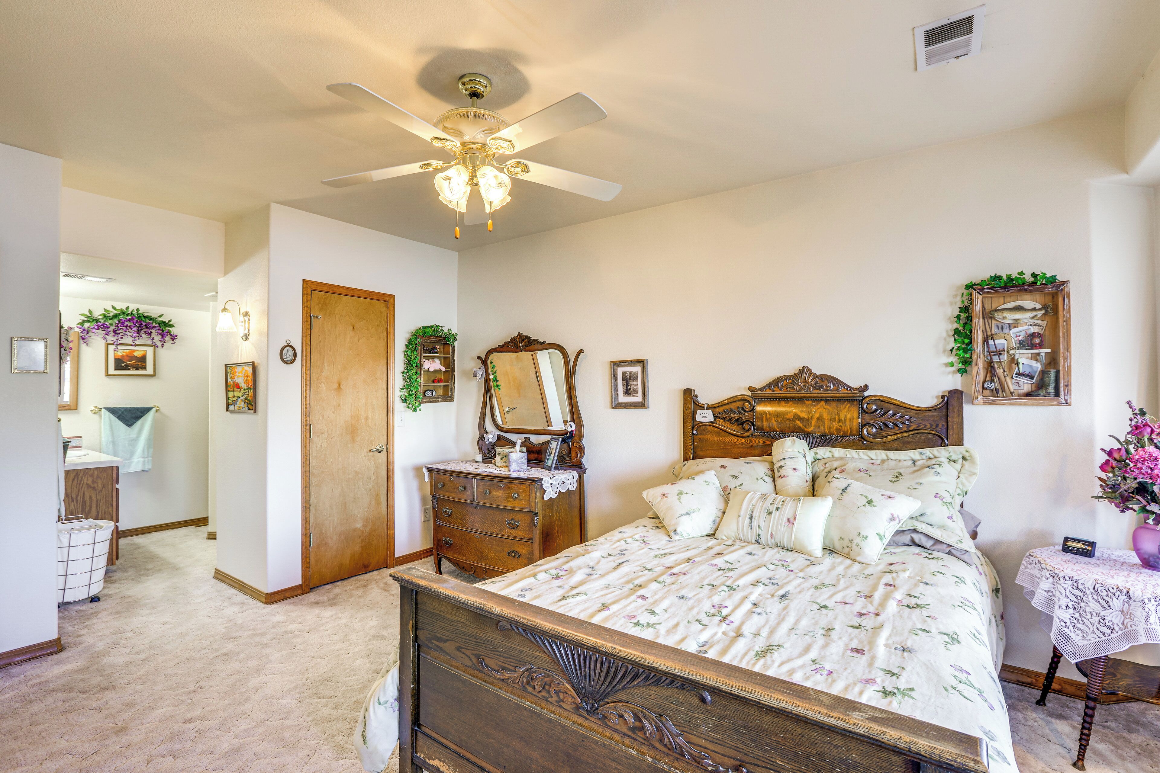 A bedroom with a wooden bed, a ceiling fan, a dresser, a mirror, and a small table with a vase of flowers.