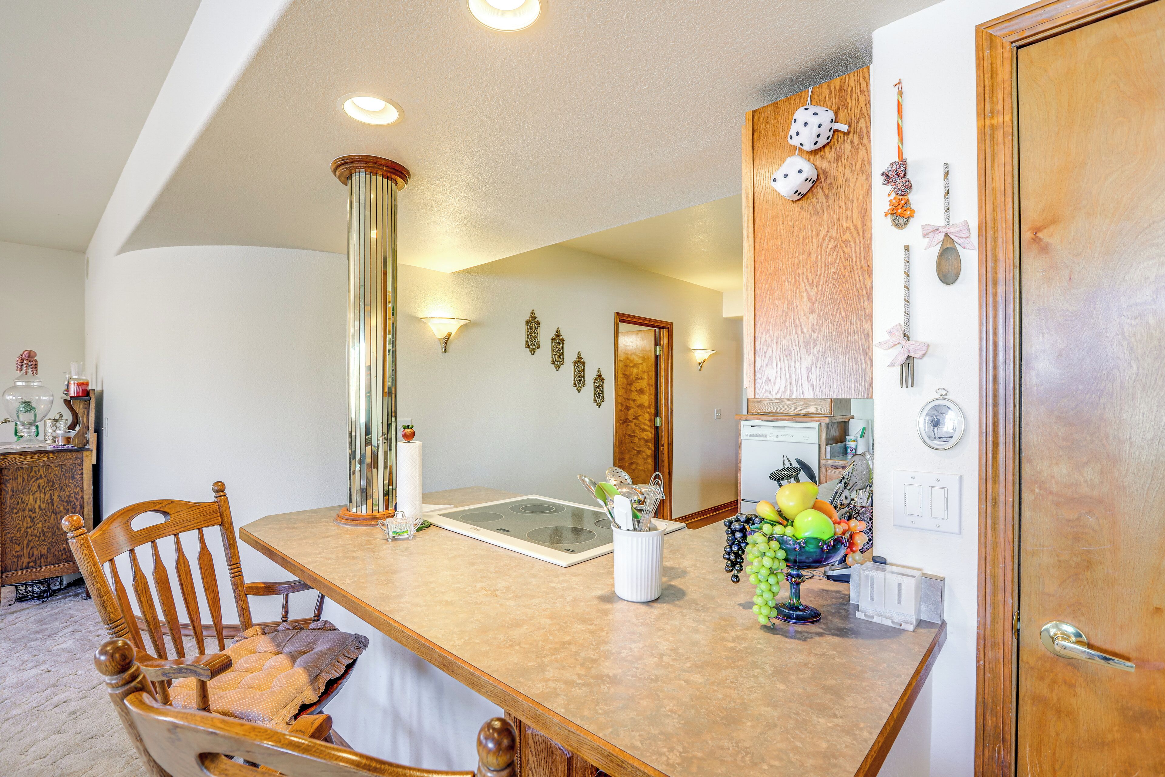 A kitchen with a wooden dining table, chairs, a vase with fruits, and wall-mounted light fixtures.