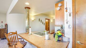 A kitchen with a wooden dining table, chairs, a vase with fruits, and wall-mounted light fixtures.