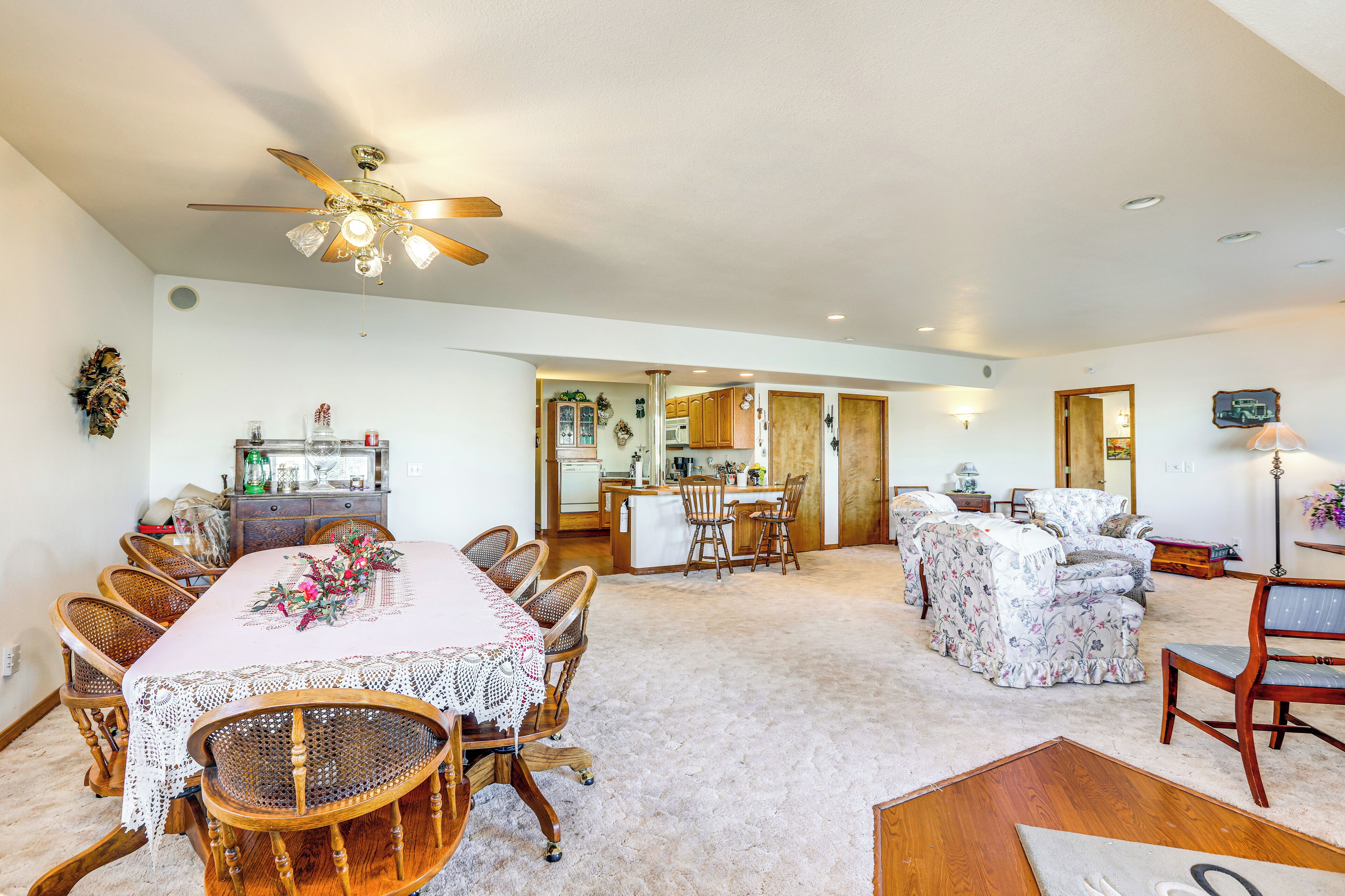 A spacious living area with a dining table, chairs, a sofa, and a kitchen in the background.