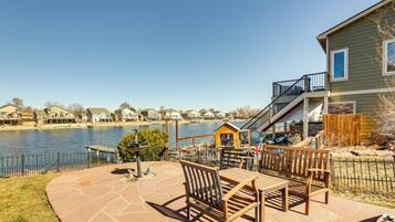 A patio with outdoor furniture overlooking a lake, a wooden deck, and a house with a staircase leading to a deck.
