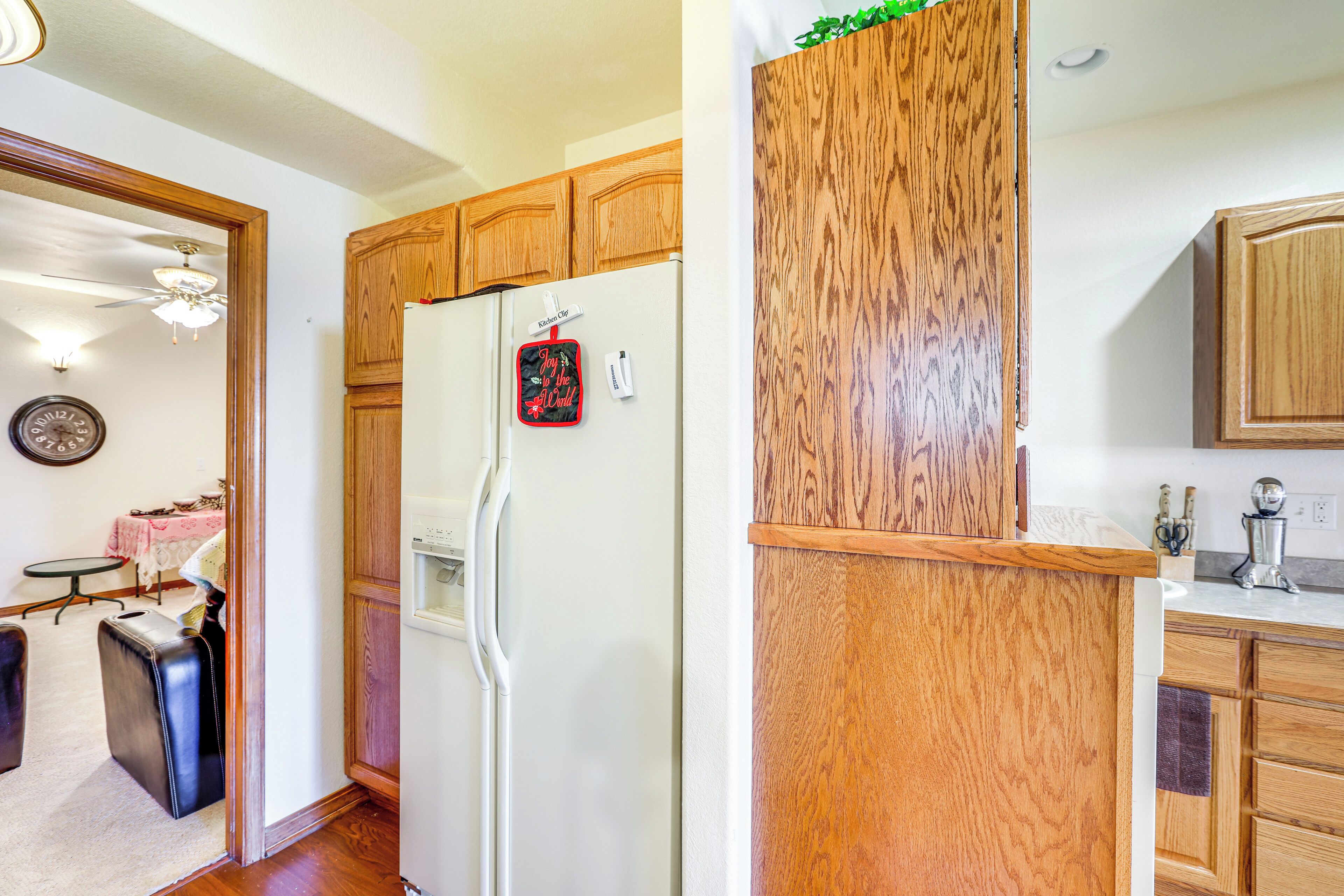 Una cocina con armarios de madera, un refrigerador blanco y una pequeña zona de comedor con mesa y sillas.