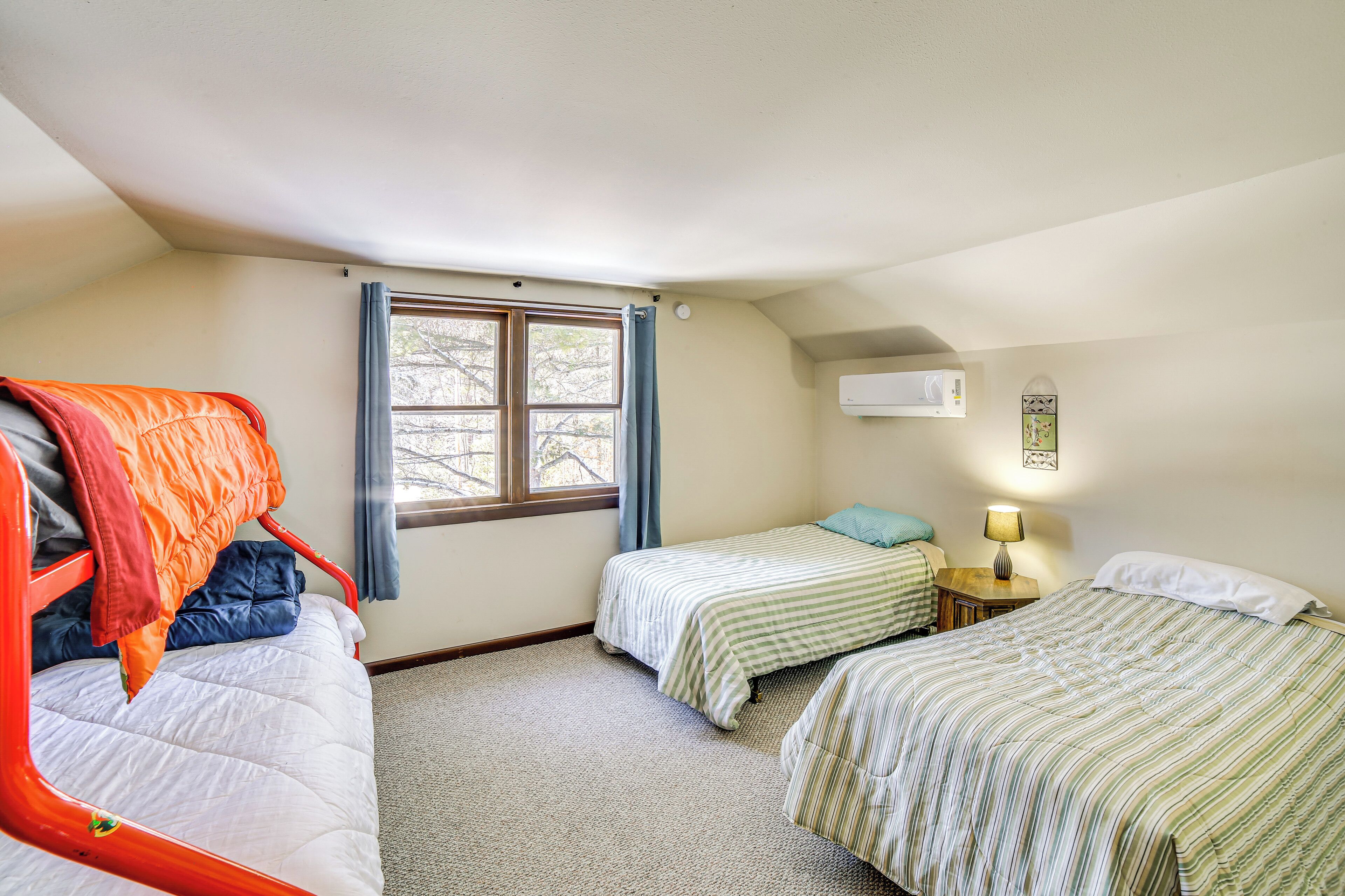 A dormitory room with two beds, a window with curtains, a bedside lamp, and an air conditioning unit.