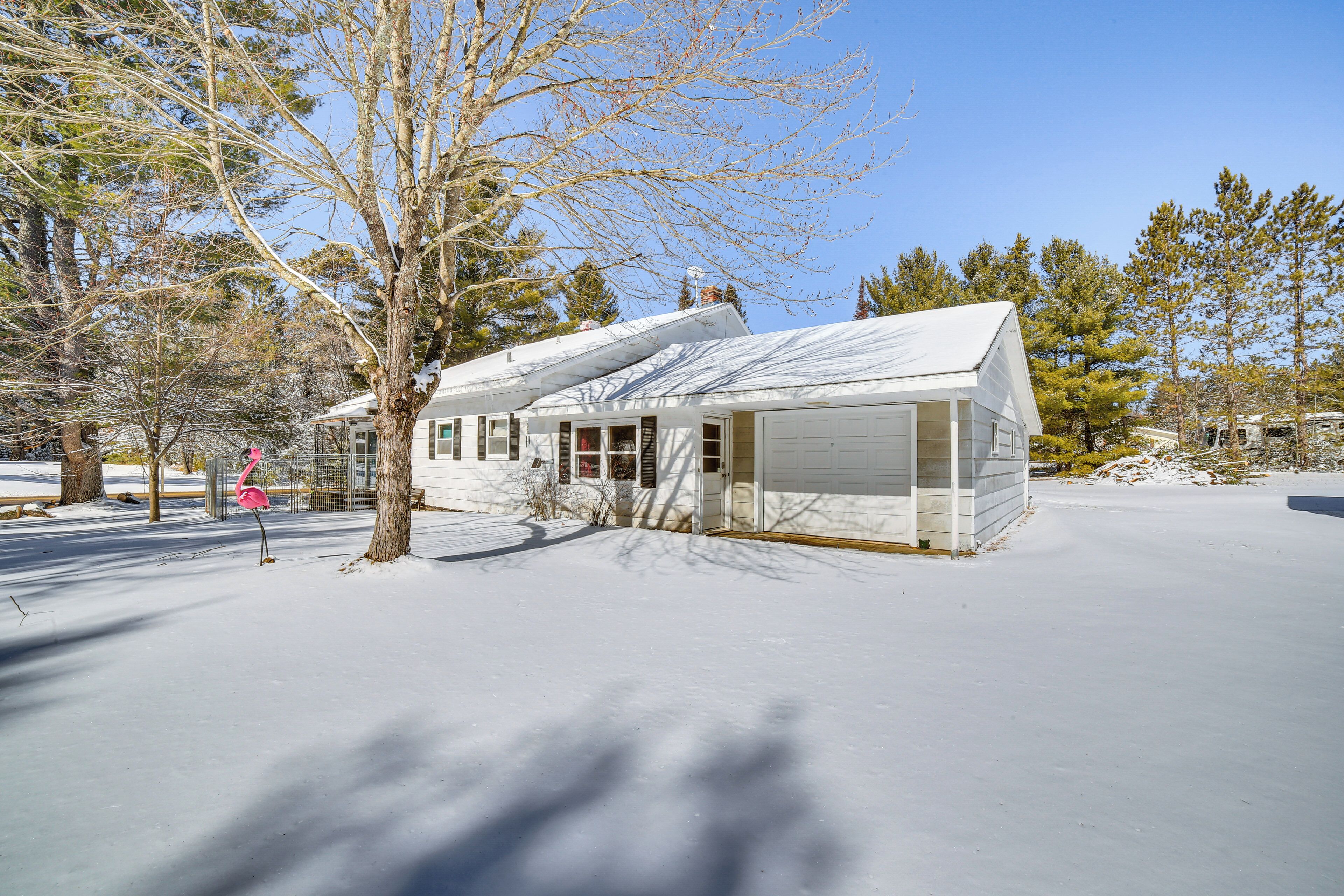 A single-story house with a garage, surrounded by snow-covered ground and trees.