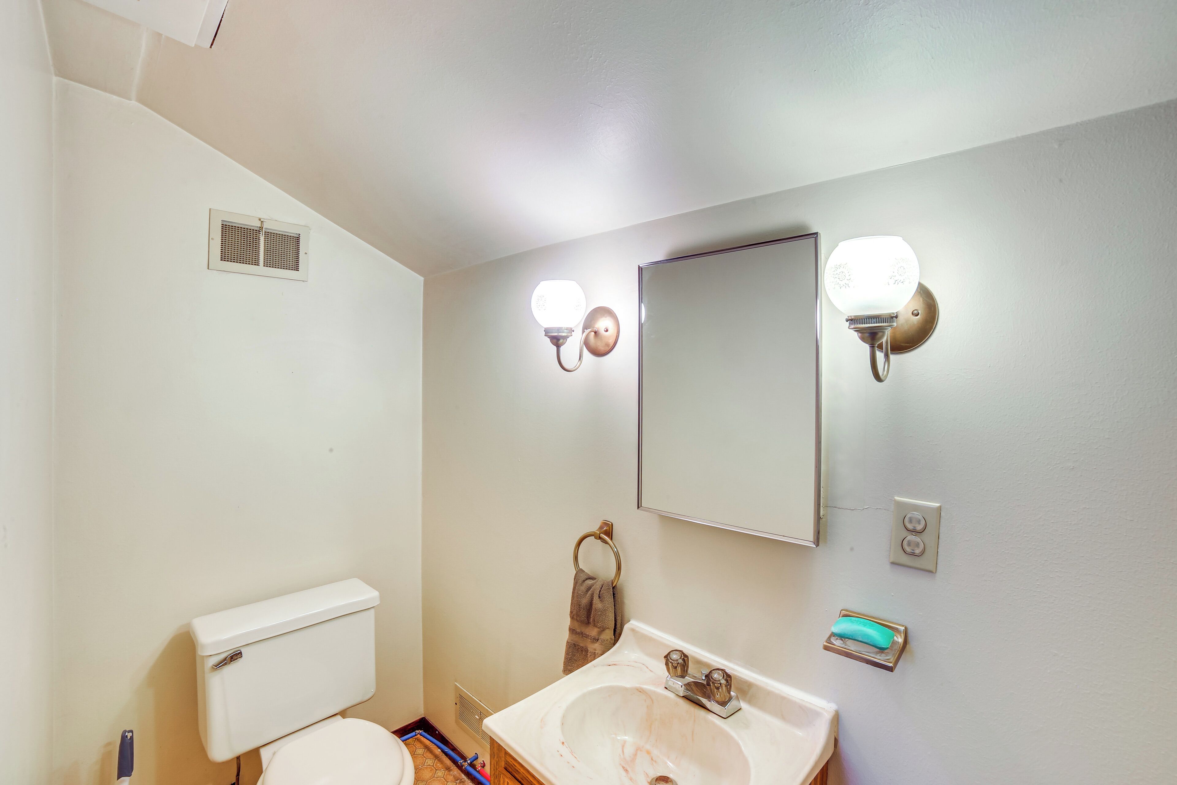 A bathroom with a toilet, sink, mirror, and two wall-mounted lights.
