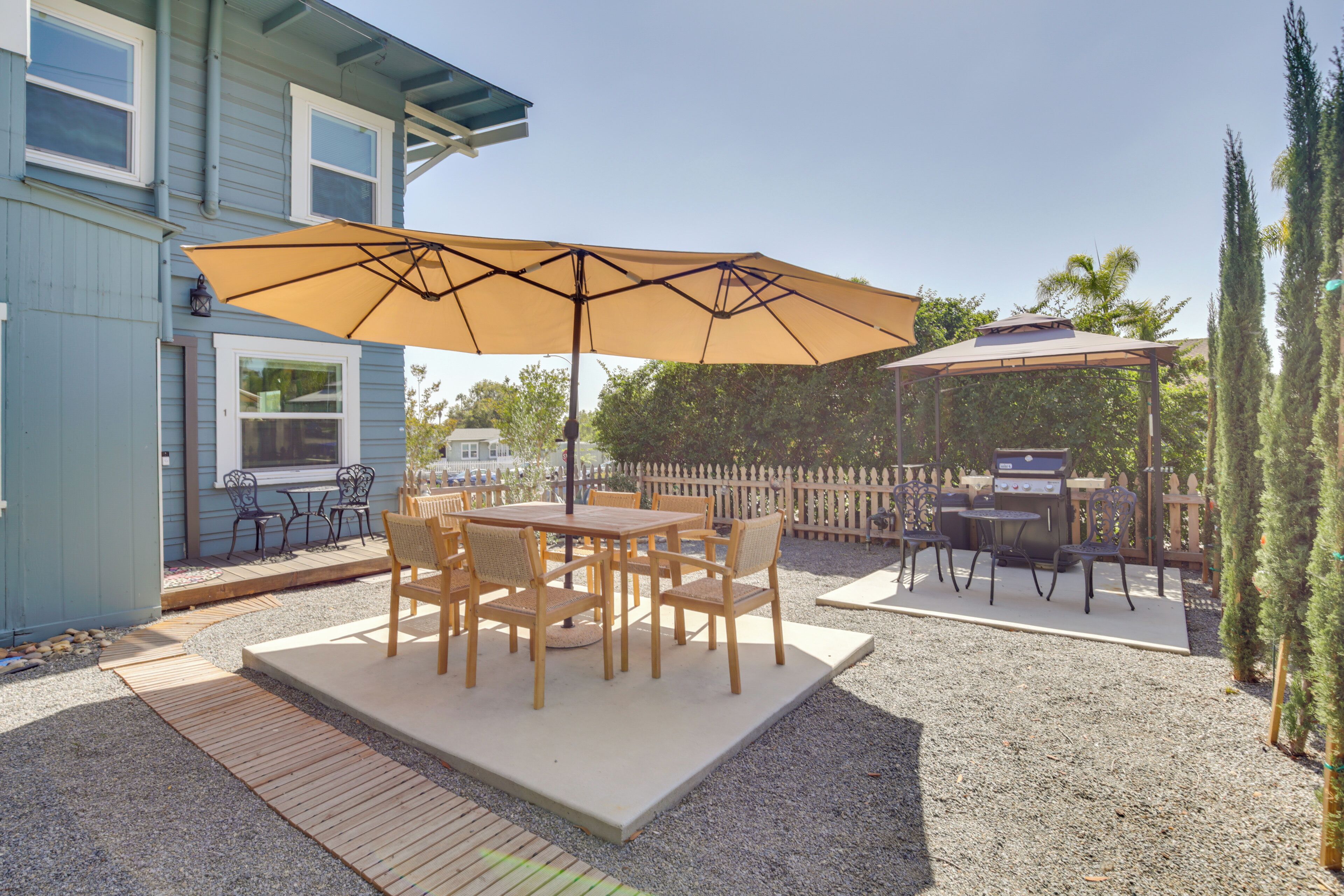Eine Terrasse im Freien mit Tisch, Stühlen, einem großen Sonnenschirm und einem Grillbereich.