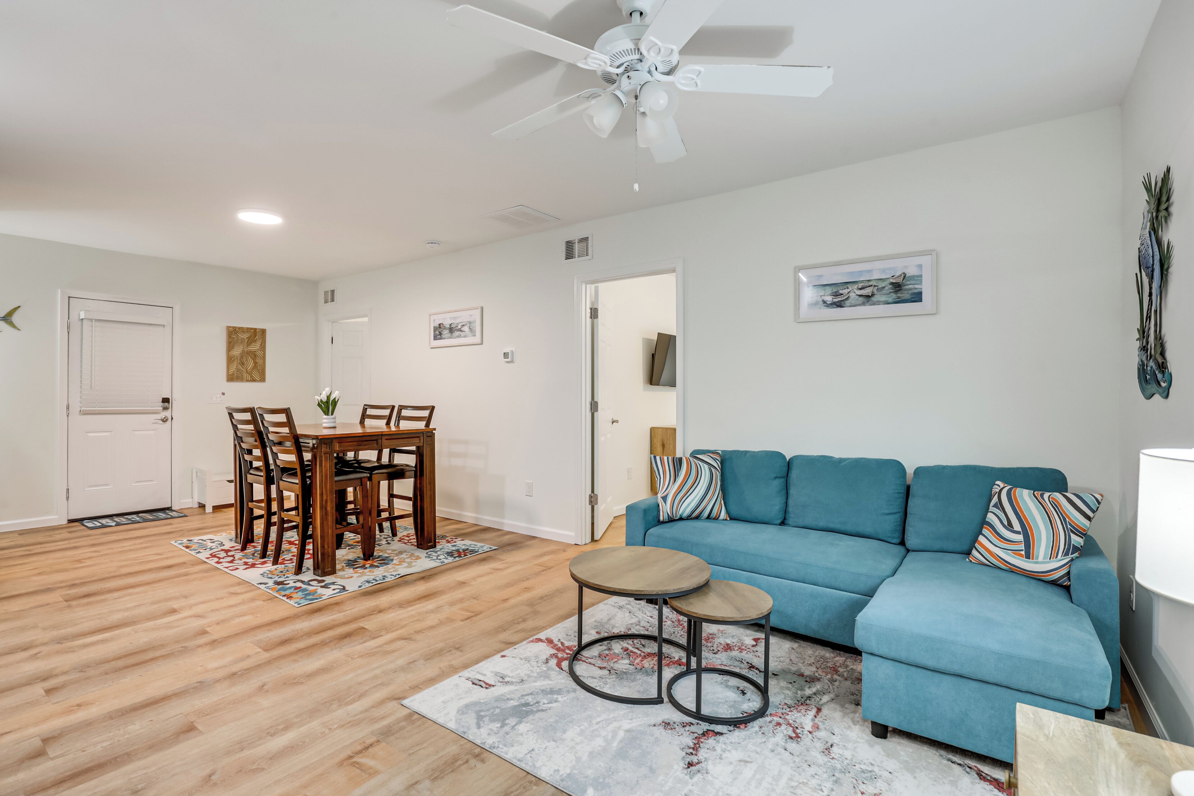 A living room with a blue sofa, a dining table with chairs, a ceiling fan, and a door.