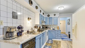 Une cuisine avec des meubles de rangement bleus, un lave-vaisselle, un four à micro-ondes et une machine à café.
