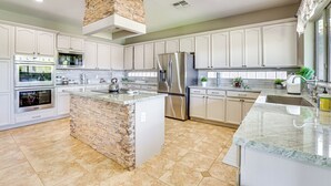 A modern kitchen with white cabinetry, a central island with a stone accent, stainless steel appliances, and a large window providing natural light. - Luxe Mtn-view Mansion w/ Hot Tub in Phoenix! (Phoenix)