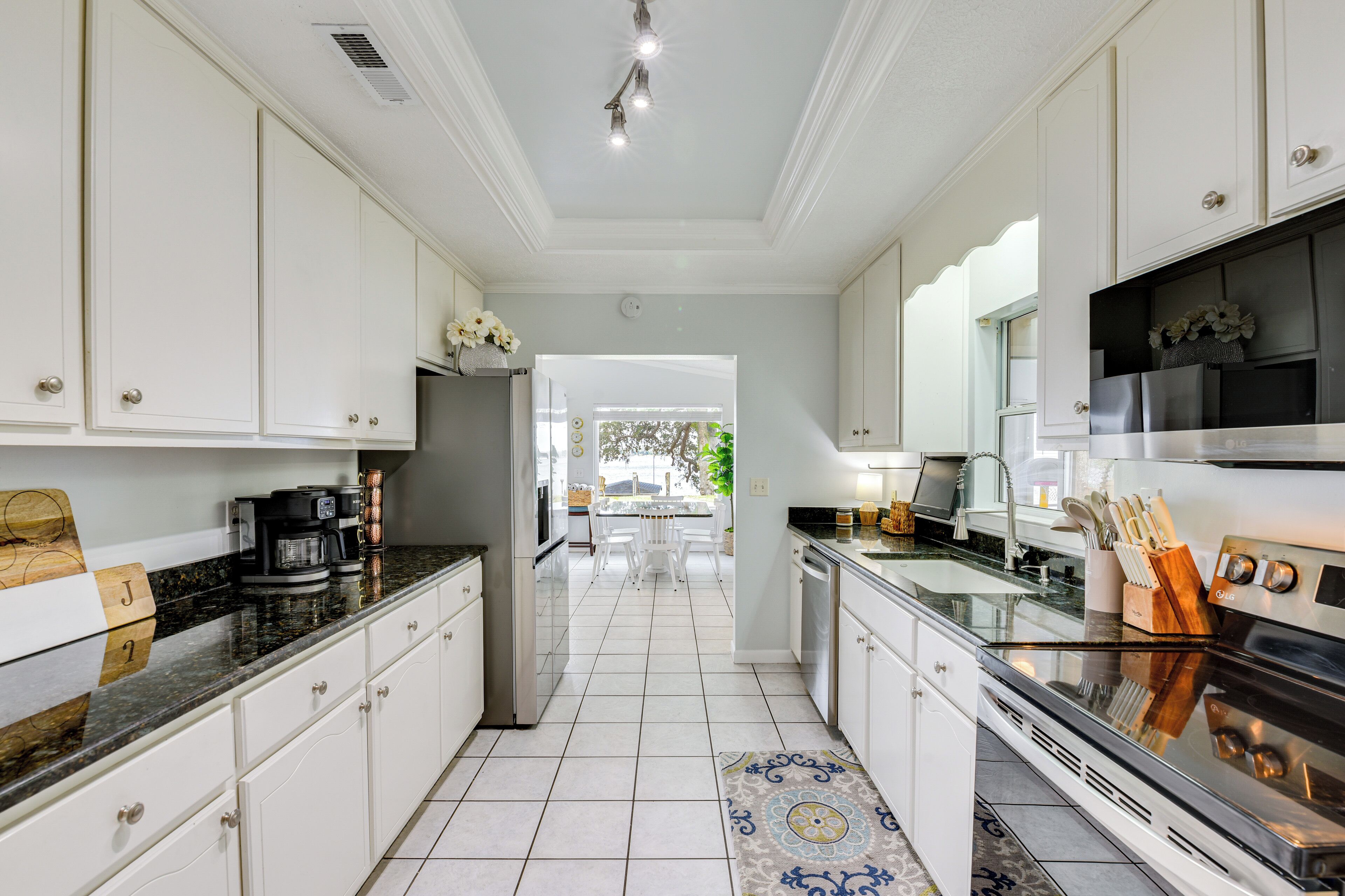 A modern kitchen with white cabinetry, a stainless steel refrigerator, and a large island with a sink and stove.