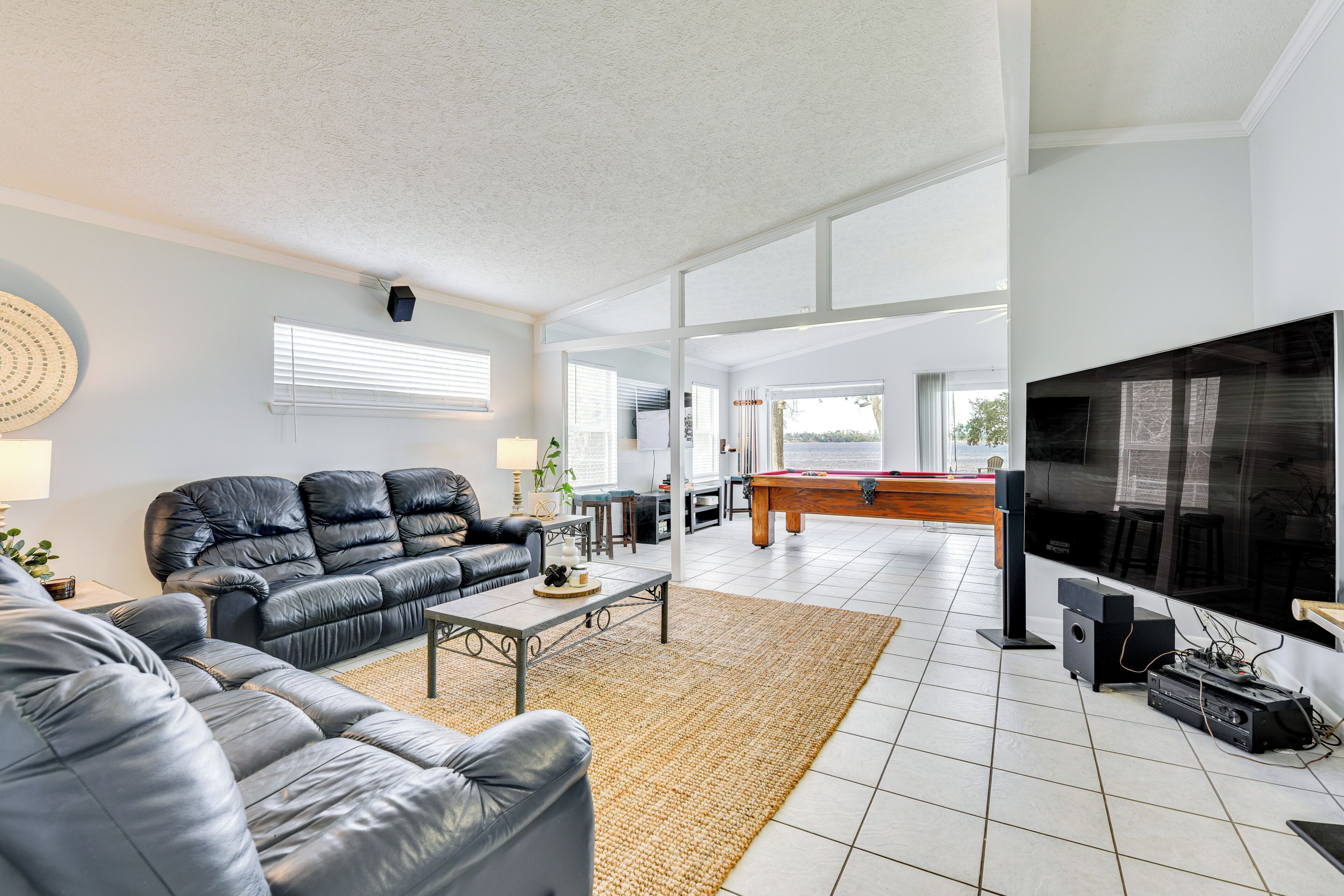 A spacious living room with a black leather sofa, a pool table, and a large flat-screen TV.