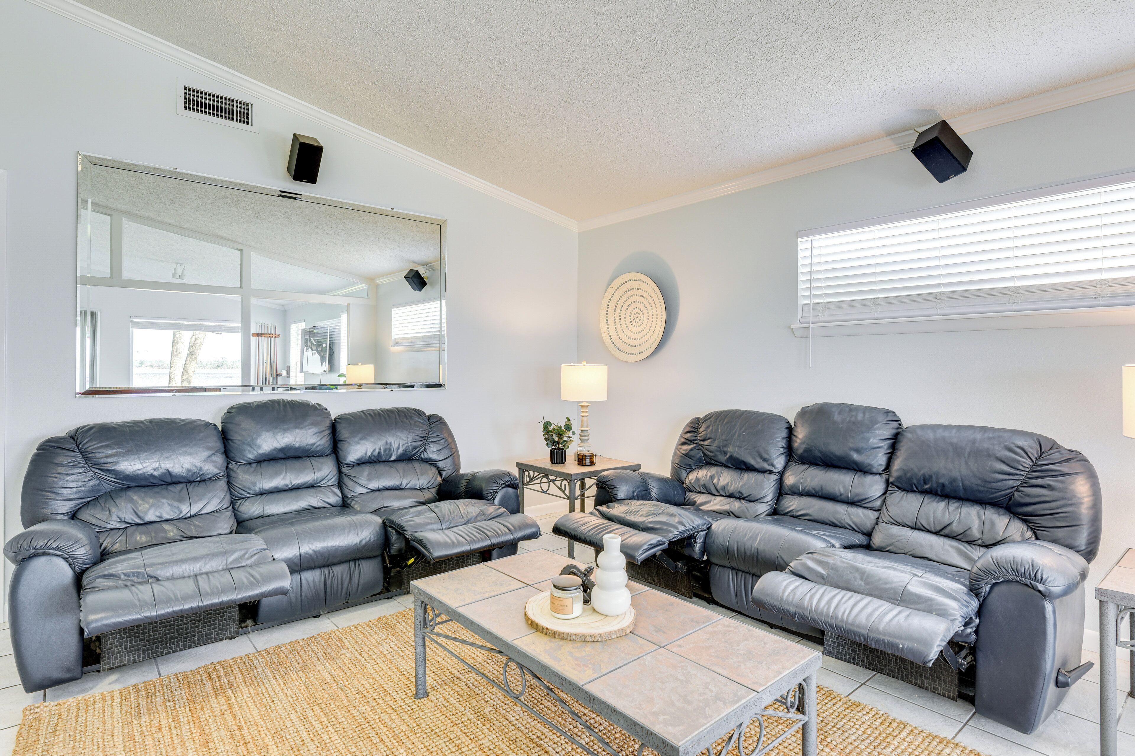 A living room with two black leather sofas, a coffee table with decorative items, a side table with a lamp, and a large mirror on the wall.