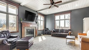 A spacious living room with leather sofas, a fireplace, and large windows offering a view of the outdoors. - 8 Mi to Lambeau Field: Family Home in De Pere! (De Pere)