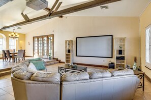 A spacious living room with a large sectional sofa, a coffee table, and a flat-screen TV mounted on the wall. There is a dining area with a table and chairs visible in the background. - 7 Mi to Las Vegas Strip: Home w/ Pool (Las Vegas)