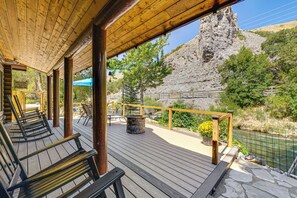 En træterrasse med udendørs møbler, en stenvæg og udsigt til en flod.