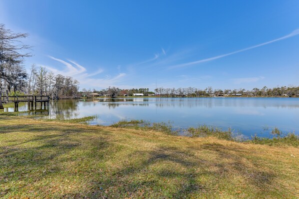 A calm lake with a wooden dock, grassy banks, and trees in the background. - Walk to Lake: Fishing Retreat in Wewahitchka (Wewahitchka)