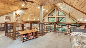 Um amplo loft com teto alto, vigas de madeira, ventilador de teto e uma grande janela com vista para o exterior.