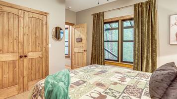 A bedroom with a large bed, a wooden wardrobe, a window with curtains, and a welcome sign.