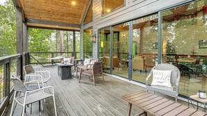 A covered outdoor area with wooden decking, wicker furniture, and a glass wall offering a view of the surrounding forest. - Lake Views & Golf Access at Secluded Drasco Lodge (Drasco)