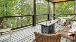 Um deck coberto ao ar livre com móveis de vime, churrasqueira e vista para a floresta circundante.