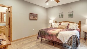 Quarto com cama, luminárias de cabeceira, ventoinha no teto, quadro na parede e porta de madeira.
