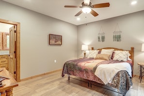 A bedroom with a bed, bedside lamps, a ceiling fan, a framed picture on the wall, and a wooden door.