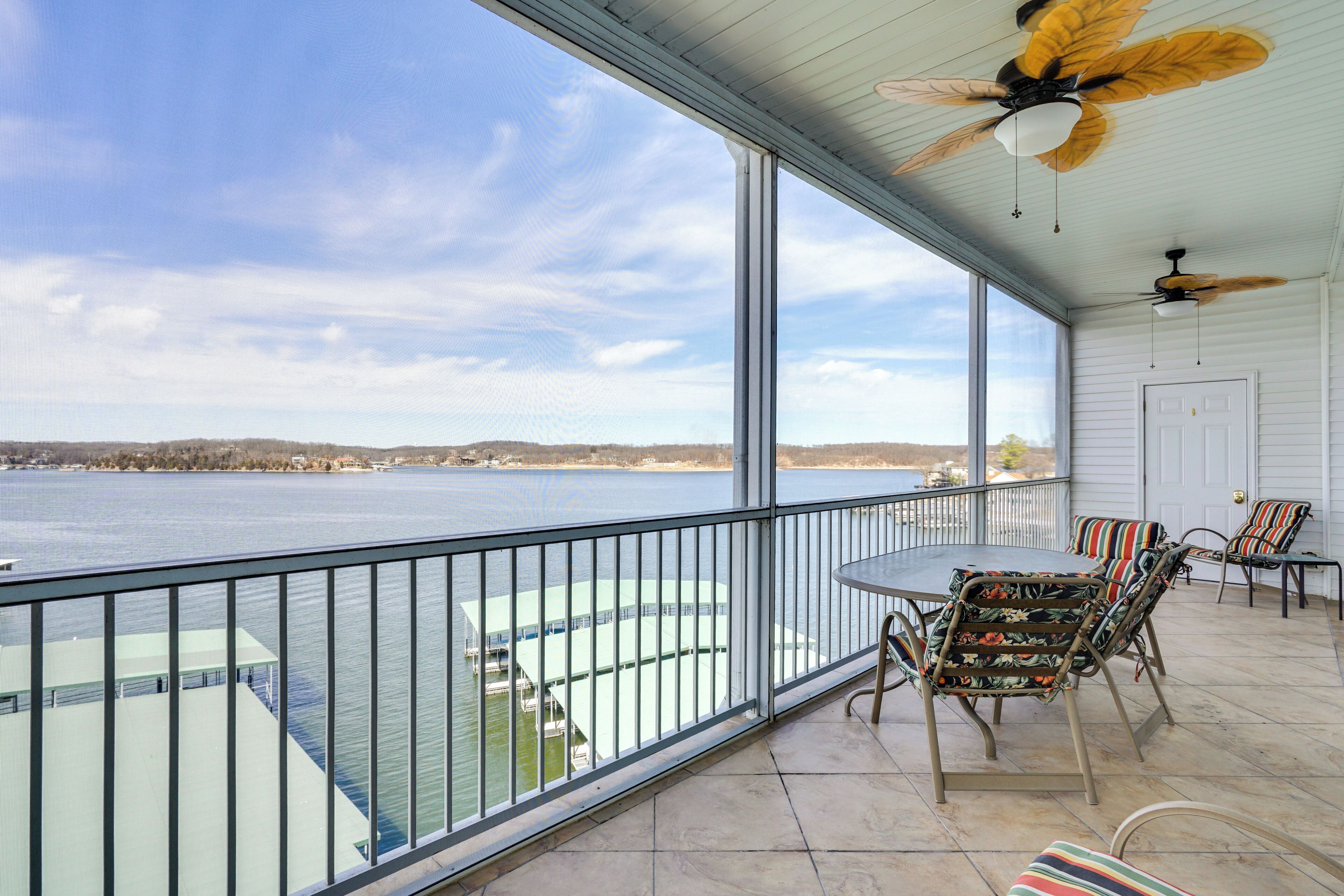 A balcony with a view of a body of water, a table, chairs, and ceiling fans.