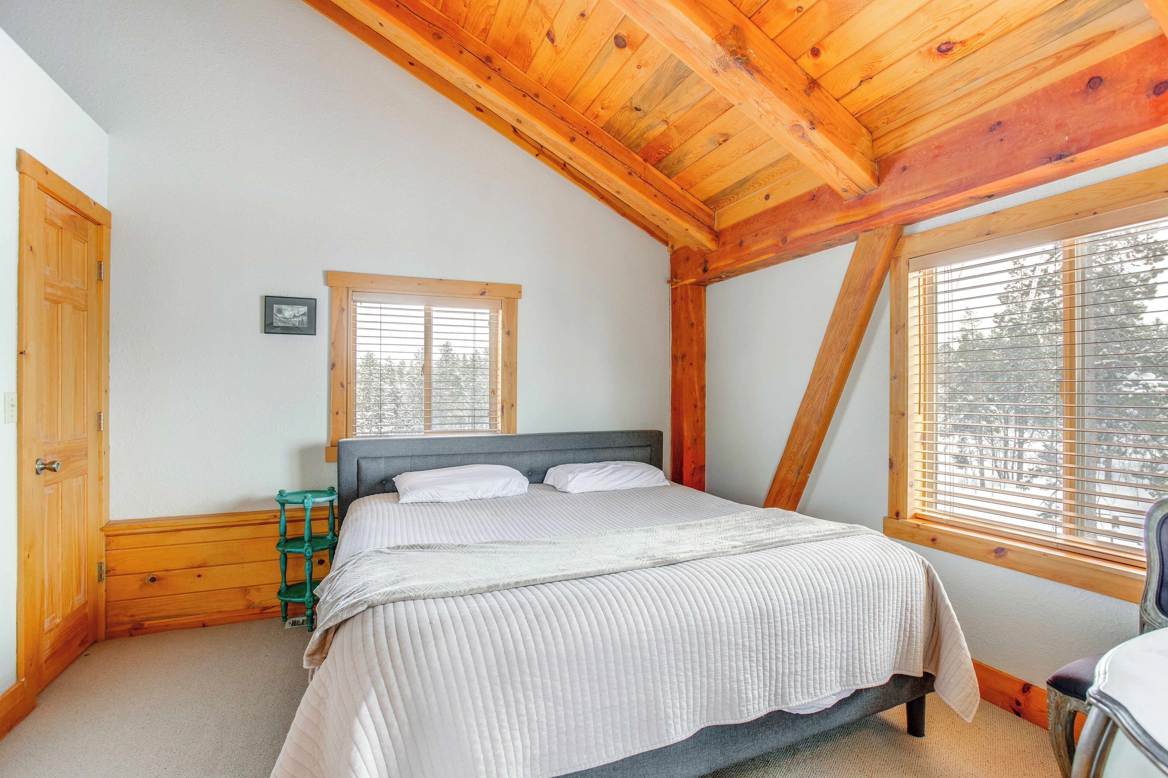 Ein Schlafzimmer mit Holzboden, einem Bett mit weißer Bettwäsche, einem kleinen Fenster und einer Tür.