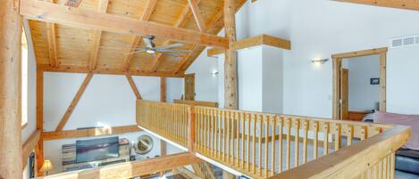 A wooden interior with a high ceiling, a staircase, and a flat-screen TV mounted on the wall.