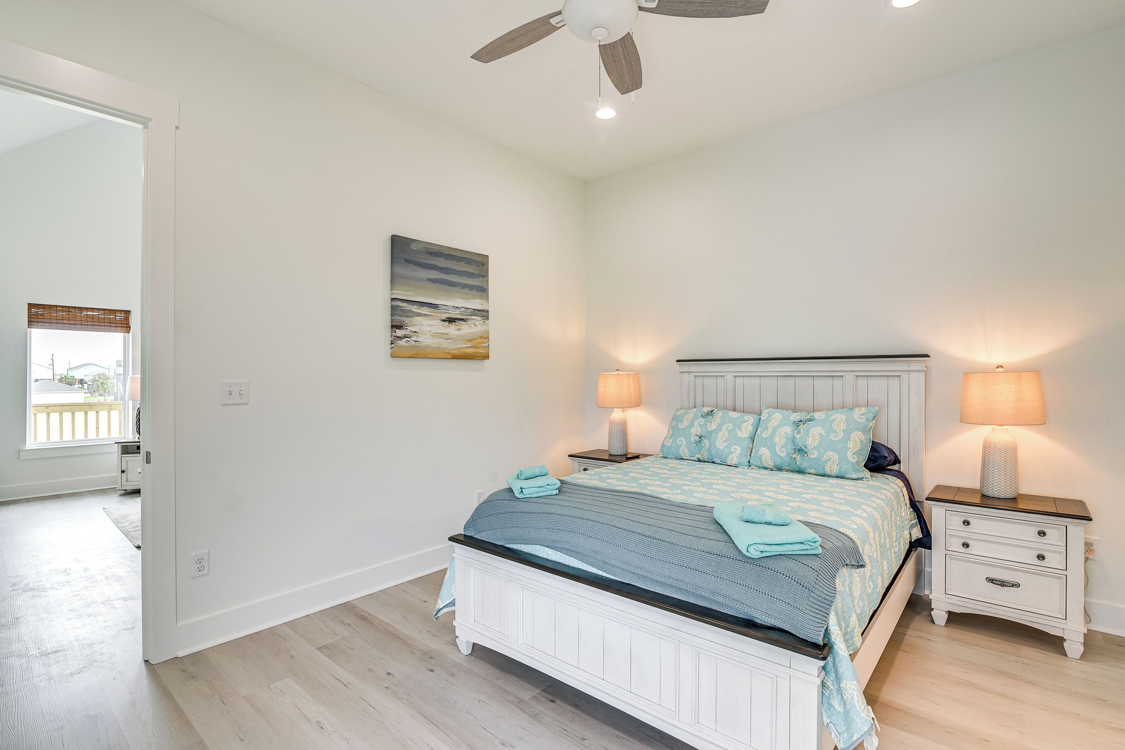 A bedroom with a bed, two bedside tables with lamps, a ceiling fan, and a painting on the wall.