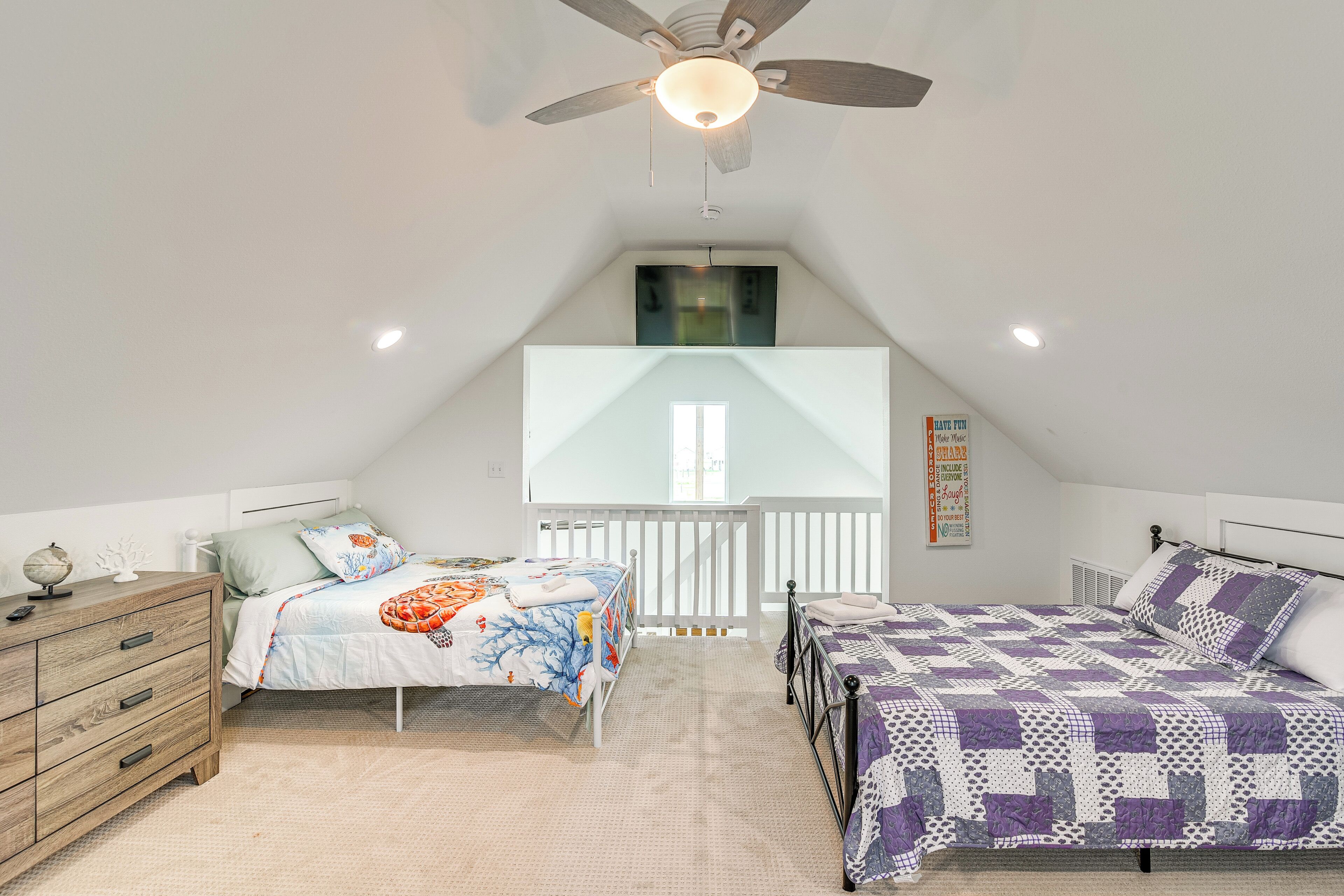 A bedroom with two beds, a ceiling fan, and a skylight.