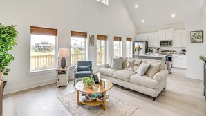A spacious living room with a high ceiling, large windows with blinds, a sofa, a coffee table, and a view of a backyard. - Walk to Crystal Beach: 'the Sandbar Escape' (Port Bolivar)