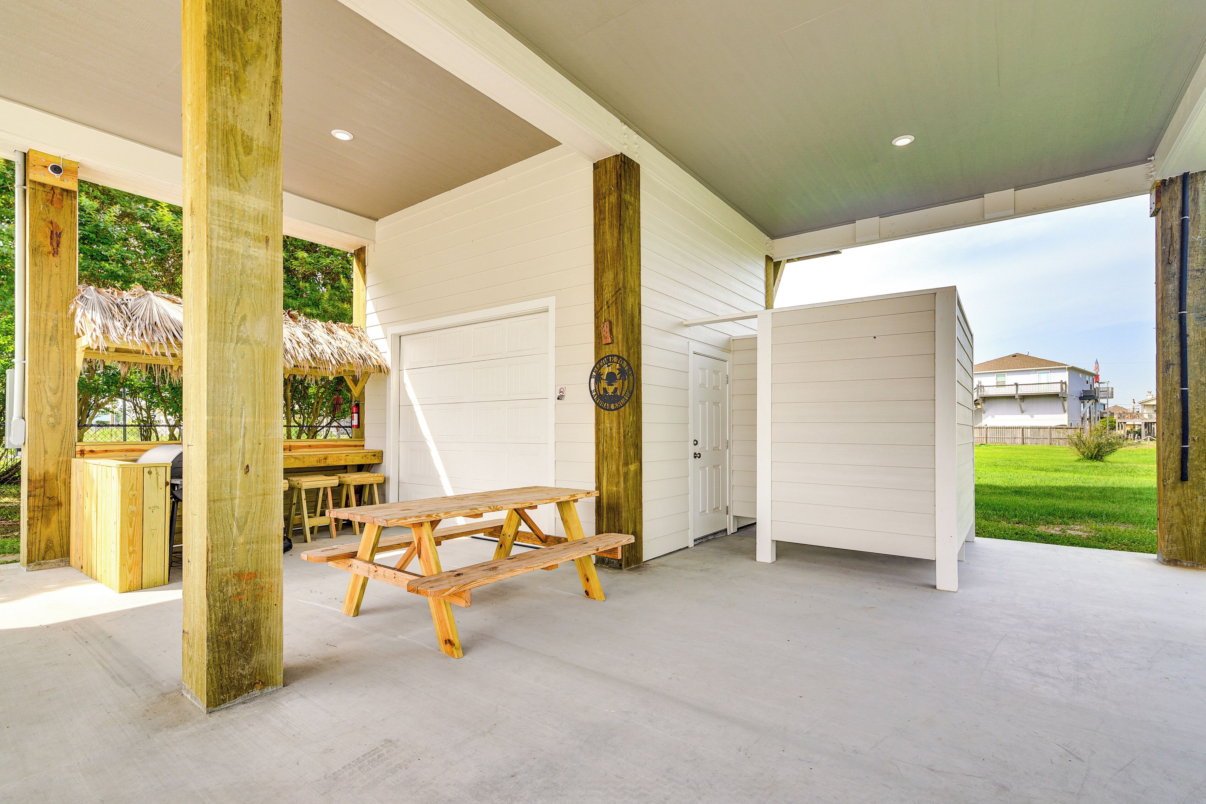 A covered patio area with a picnic table, wooden posts, and a white garage door.