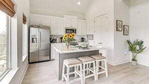 A modern kitchen with white cabinets, stainless steel appliances, and a central island with stools. - Walk to Crystal Beach: 'the Sandbar Escape' (Port Bolivar)