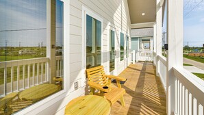 A wooden deck with a wooden chair and table, white railings, and large windows overlooking a grassy area. - Walk to Crystal Beach: 'the Sandbar Escape' (Port Bolivar)