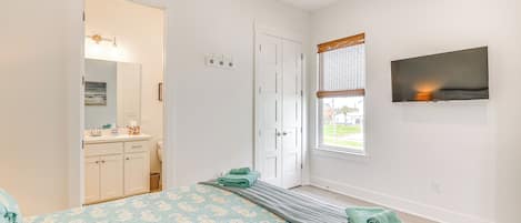 A bedroom with a bed, a TV, a window, and a bathroom visible through an open door.